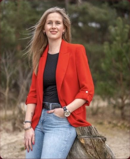 Aniek van Berkum in een rood colbert, buiten in de natuur