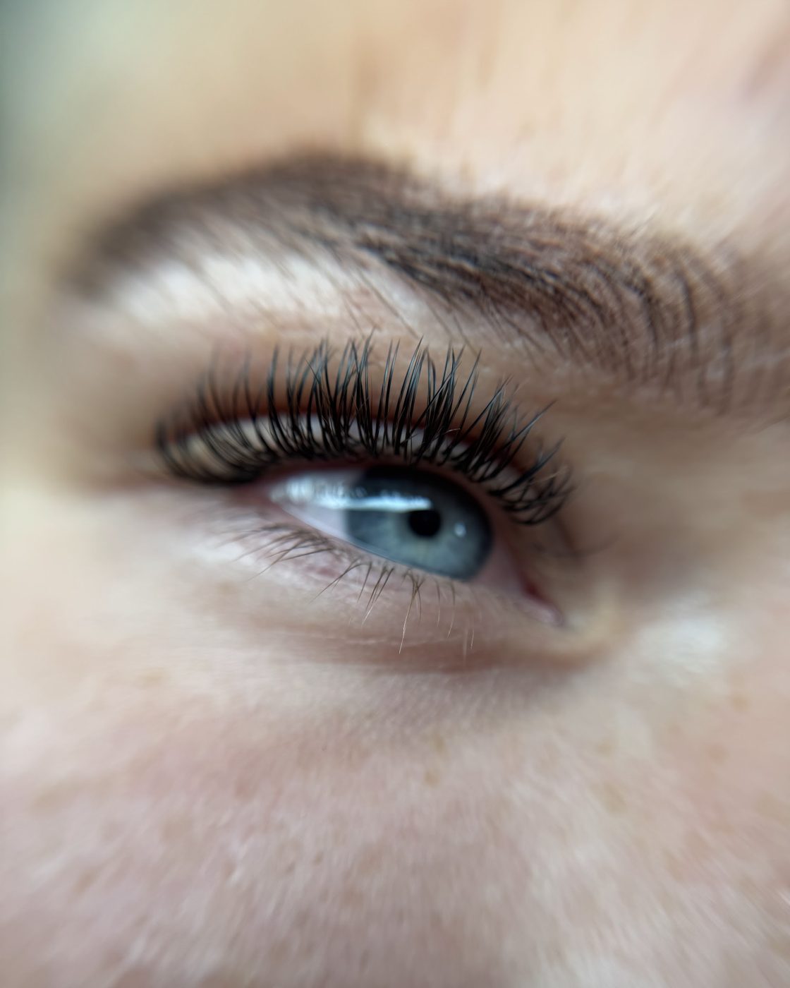Close-up van een oog met volle, donkere wimperextensions en een verzorgde wenkbrauw