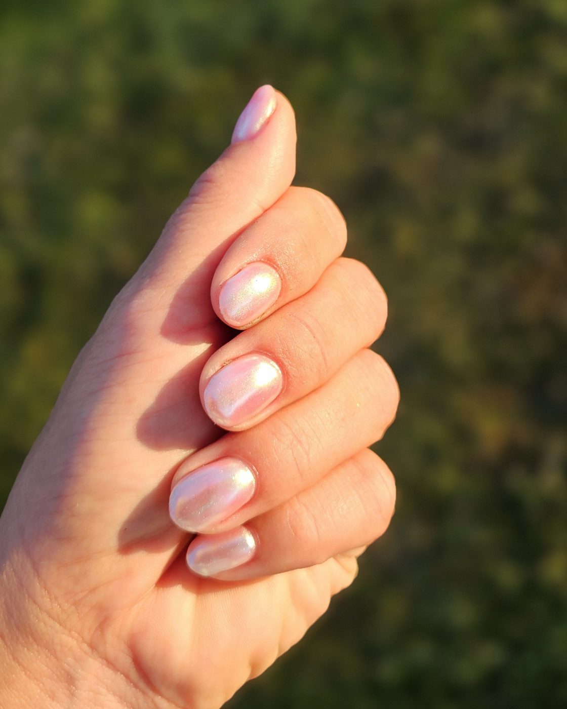 Hand met melkroze, glanzende nagels in de zon