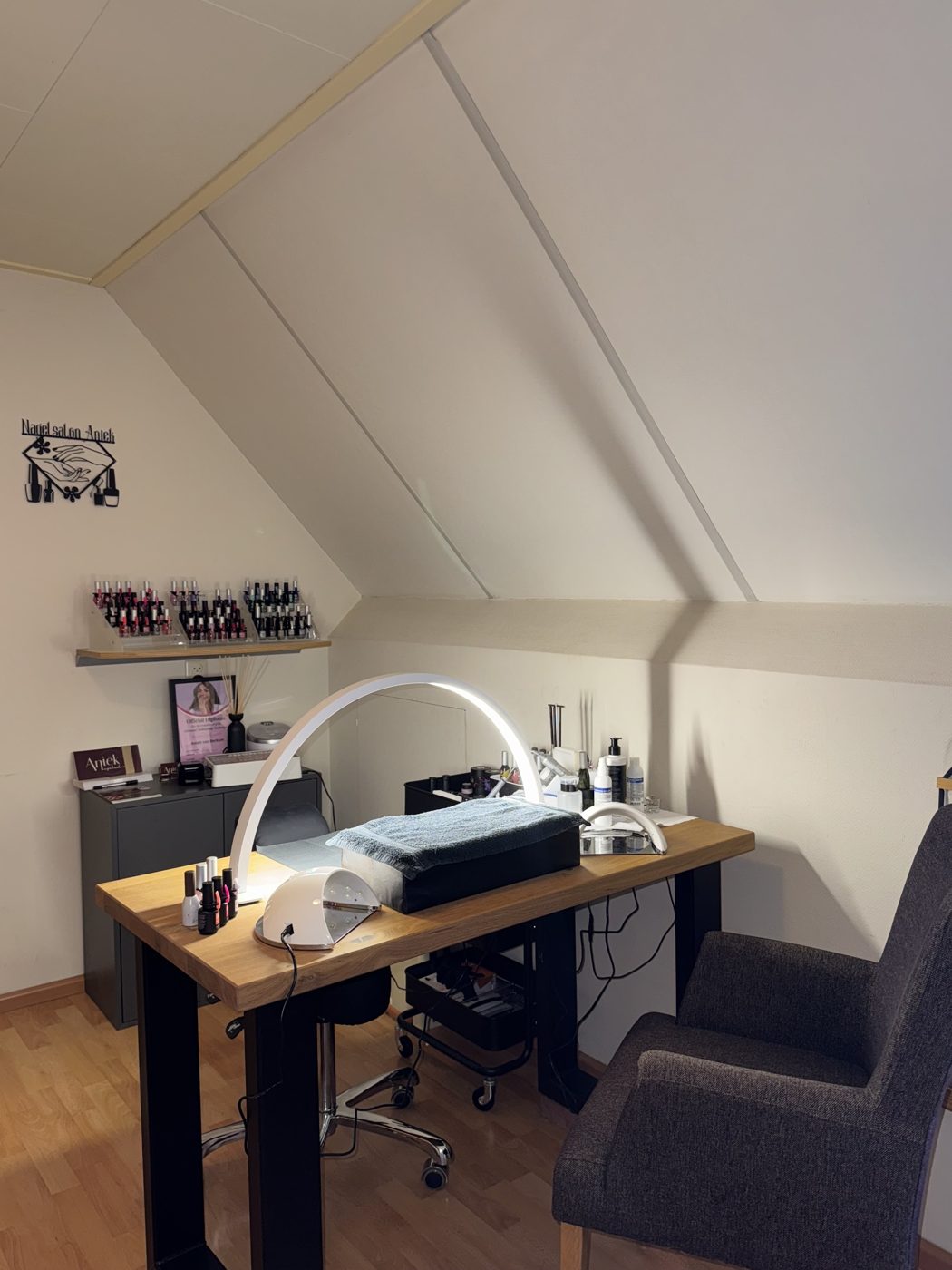 De salon onder het schuine dak: een werktafel met nagellamp, een stoel en het naambord aan de wand