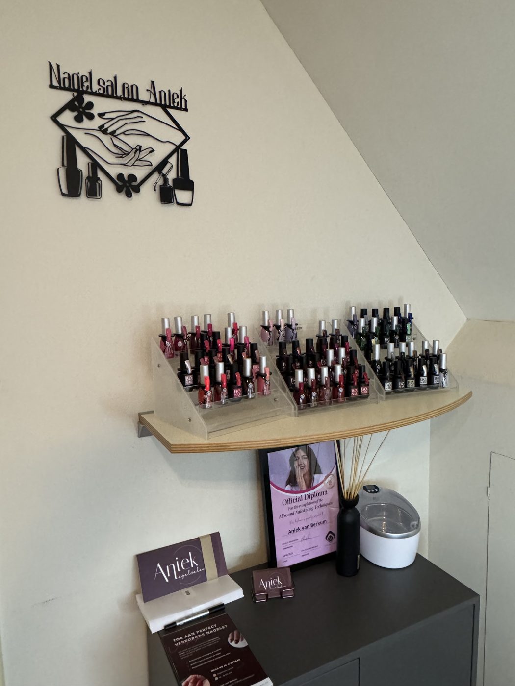 De wand in de salon: het metalen naambord van Nagelsalon Aniek boven een rek vol nagellak
