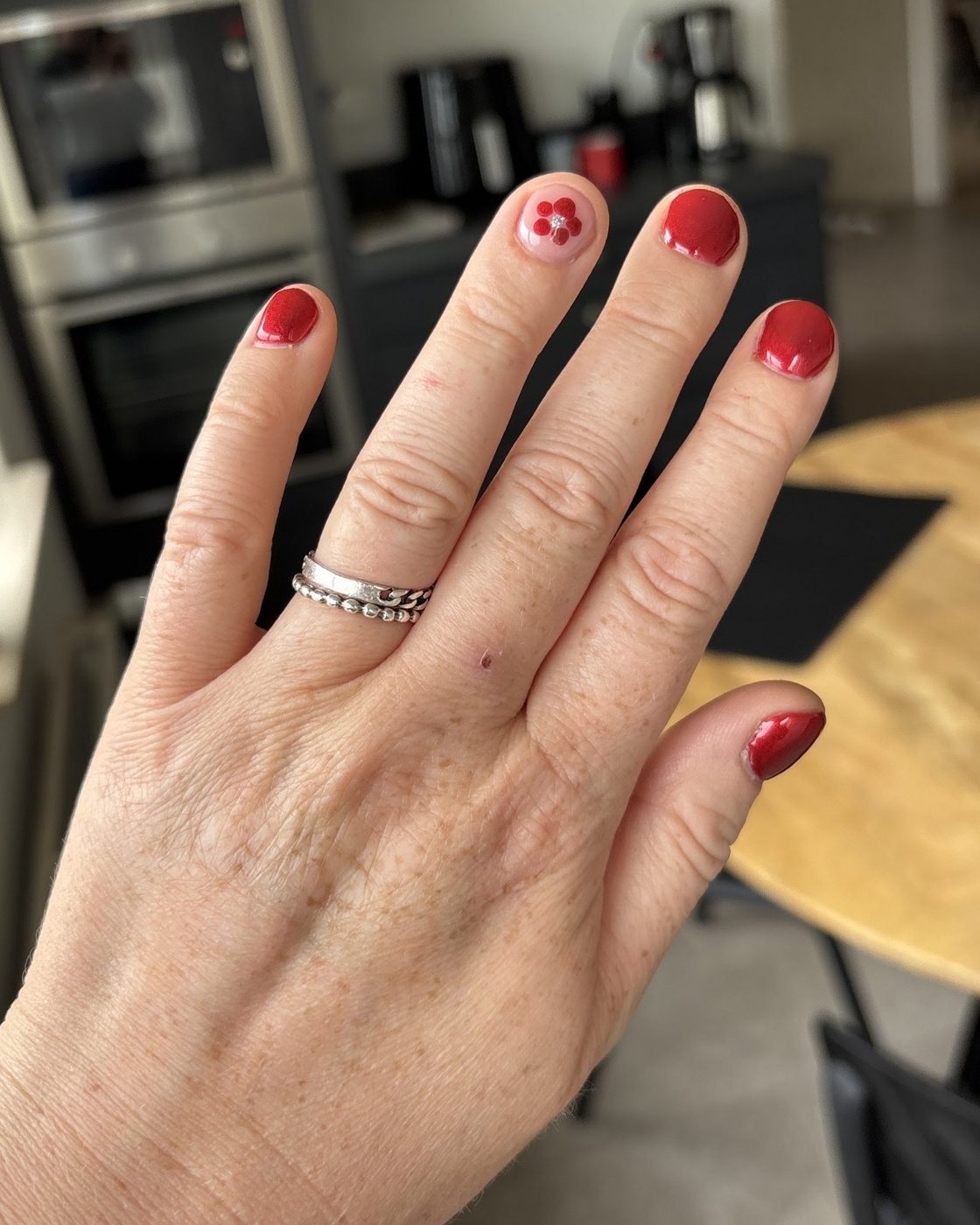 Rode gelpolish met een klein bloemetje op één nagel